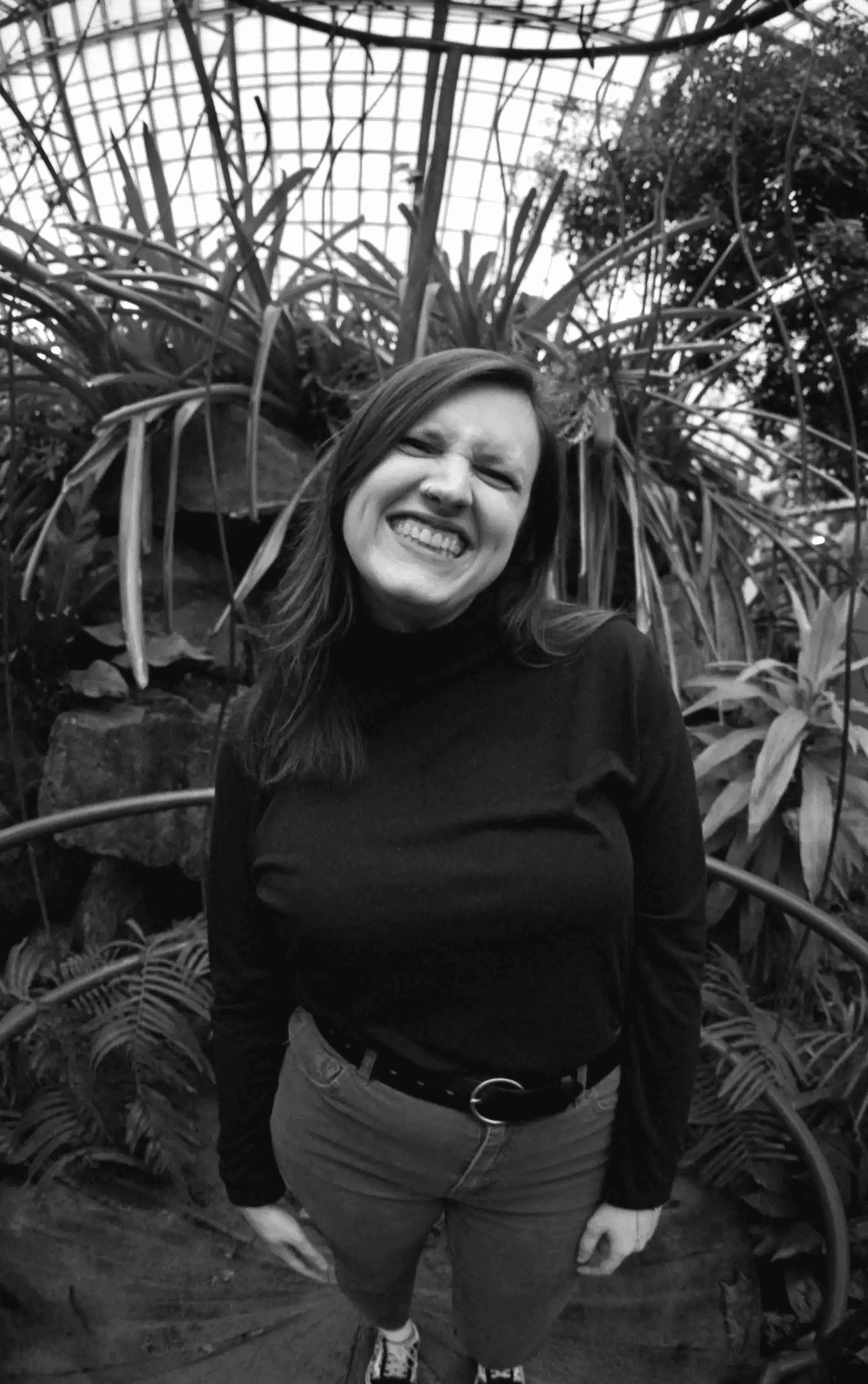 black and white photo of Megan smiling big among plants in a conservatory